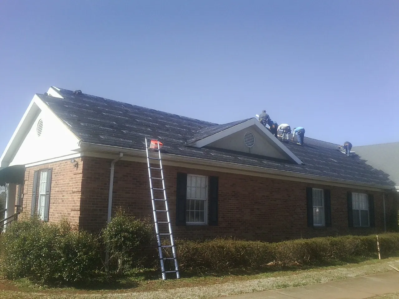 Crew tearing shingles off a brick ranch roof with a ladder set — Metal Roof Repair work by our crew in Satellite Beach