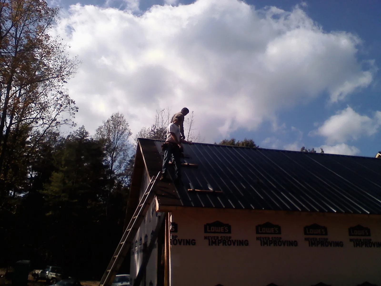 Roofer fastening dark metal panels high against a cloudy sky, from a Roof Inspection job in Satellite Beach