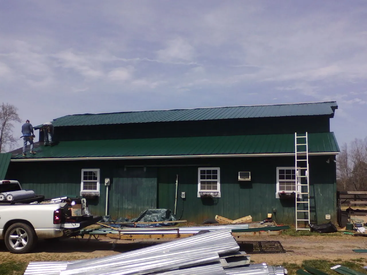 Crew installing green metal roofing on a large green barn in Satellite Beach