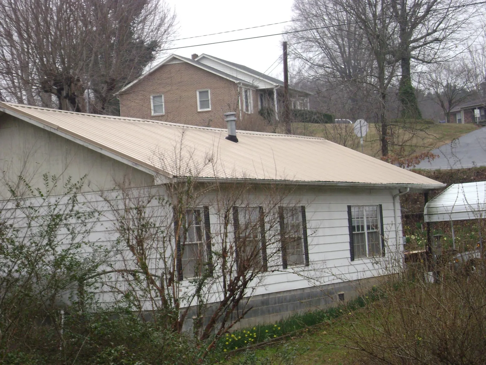 Tan metal roof on a white sided house set into a hillside — Commercial Roofing by Roofing Brothers in Satellite Beach