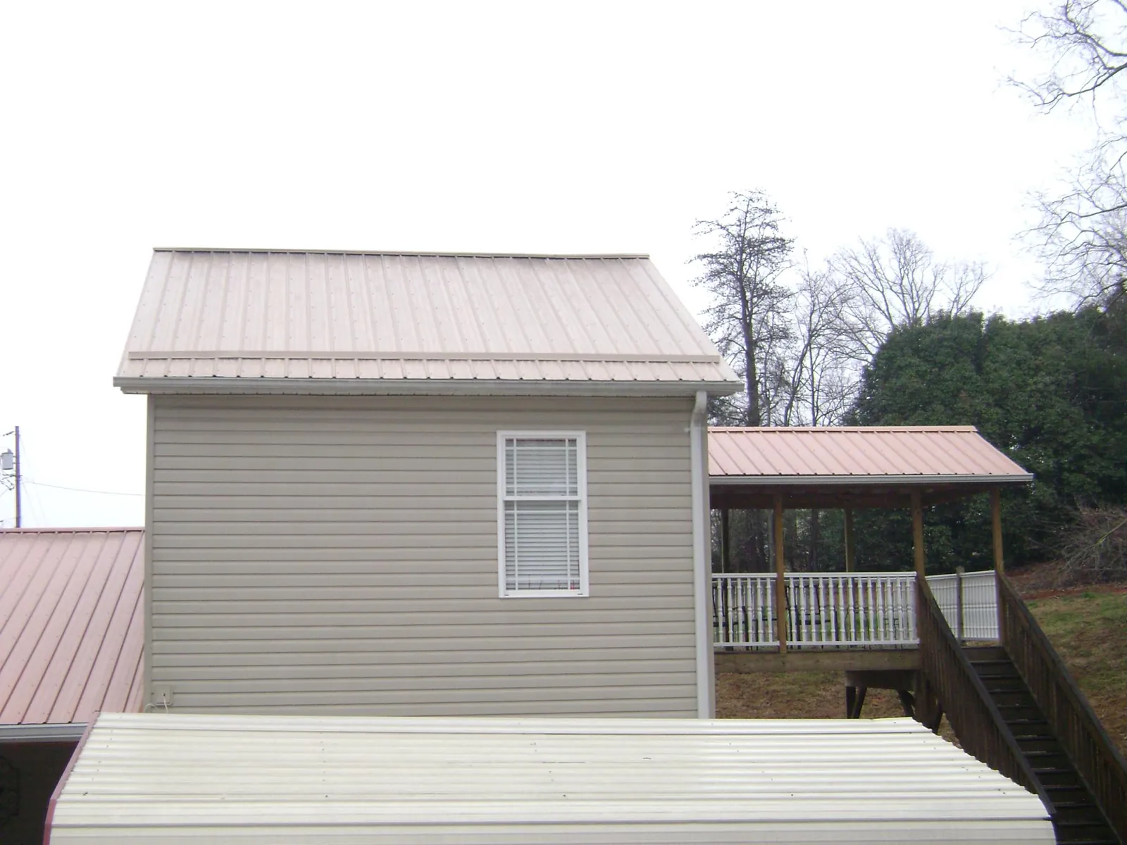 Tan metal roofs on a two story addition and attached porch, from a Roof Replacement job in Satellite Beach
